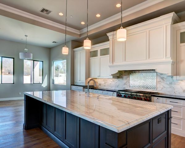 Modern luxury kitchen featuring a large dark wood island with a white marble countertop and three pendant lights hanging from a high ceiling.