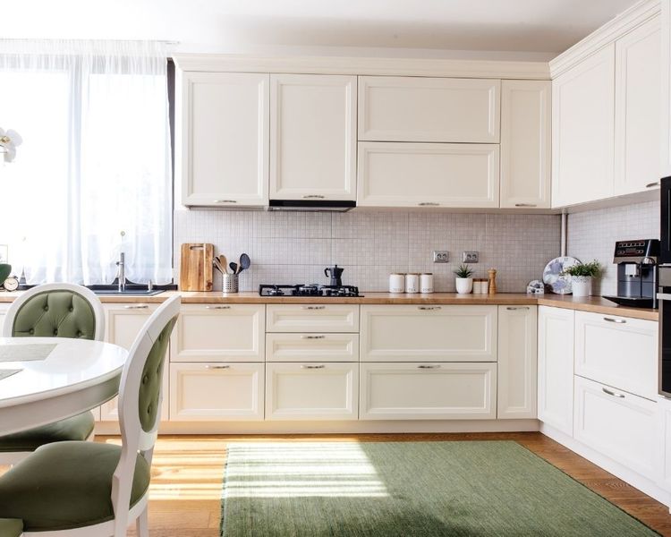 A clean, sunlit kitchen with cream-colored cabinetry, light wood countertops, a white tile backsplash, and a green rug on the floor. A clean, sunlit kitchen with cream-colored cabinetry, light wood countertops, a white tile backsplash, and a green rug on the floor.