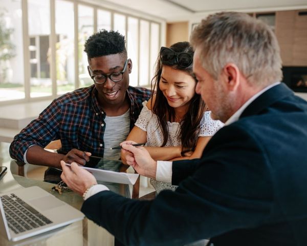 A professional consultant in a suit reviewing a document with a young couple during a home renovation consultation.