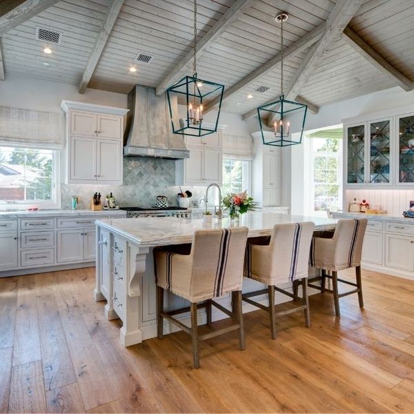 A spacious kitchen with vaulted rustic wood ceilings, white cabinetry, and a large marble island with three tan upholstered bar stools. A spacious kitchen with vaulted rustic wood ceilings, white cabinetry, and a large marble island with three tan upholstered bar stools.
