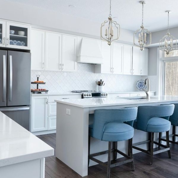 A bright, airy white kitchen featuring an island with light blue upholstered bar stools and elegant lantern-style pendant lights. A bright, airy white kitchen featuring an island with light blue upholstered bar stools and elegant lantern-style pendant lights.