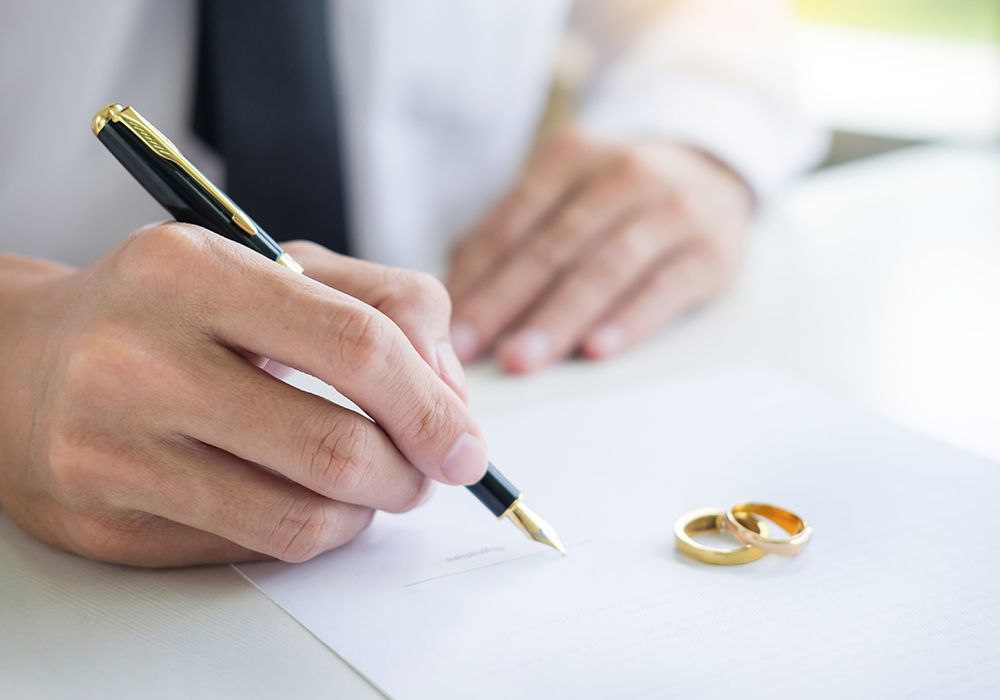 a person signing paperwork with wedding bands sitting on the papers