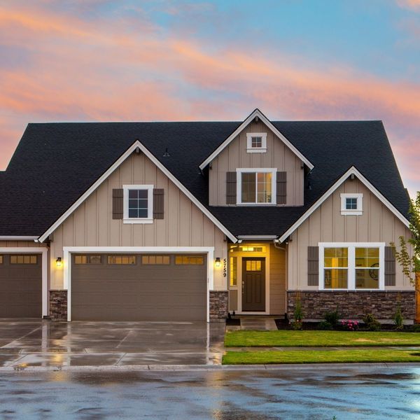 The front exterior of a charming single-story house with beige siding, dark trim, and a prominent front door, illuminated by warm evening light with a vibrant sunset sky.