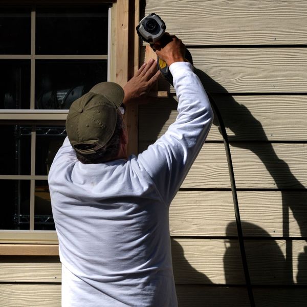 man drilling siding into house