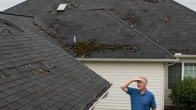 Rooftop view showing several warning signs like cracked shingles and a sagging section, with a concerned homeowner looking up from the ground.