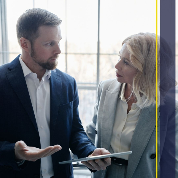 Two people collaborating and looking at a tablet screen, representing support and training for a software system. Two people collaborating and looking at a tablet screen, representing support and training for a software system.
