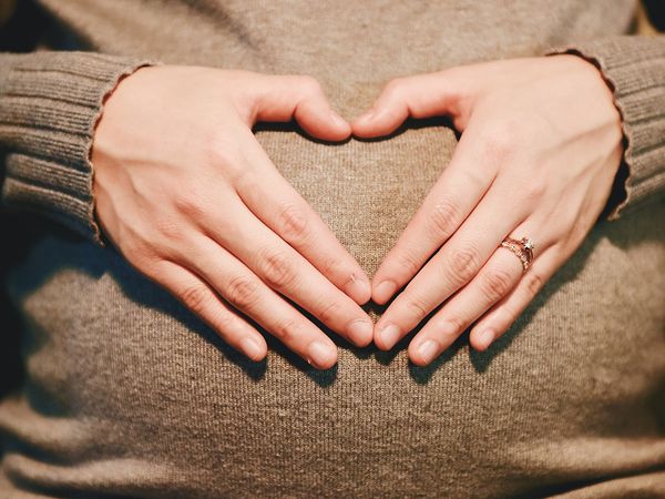 woman creating a heart shape with her hands on her pregnant belly