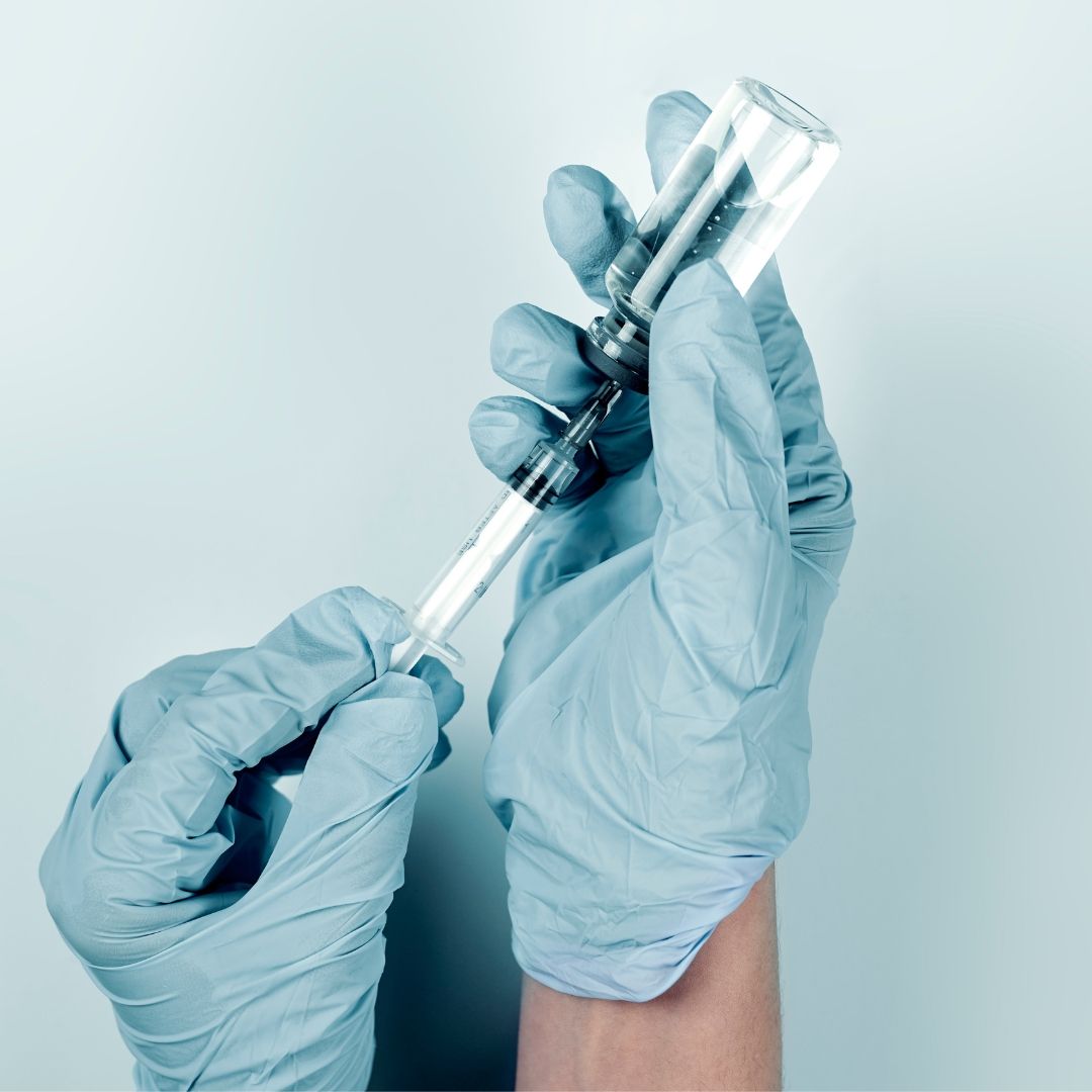 a person holding a syringe while wearing blue gloves.