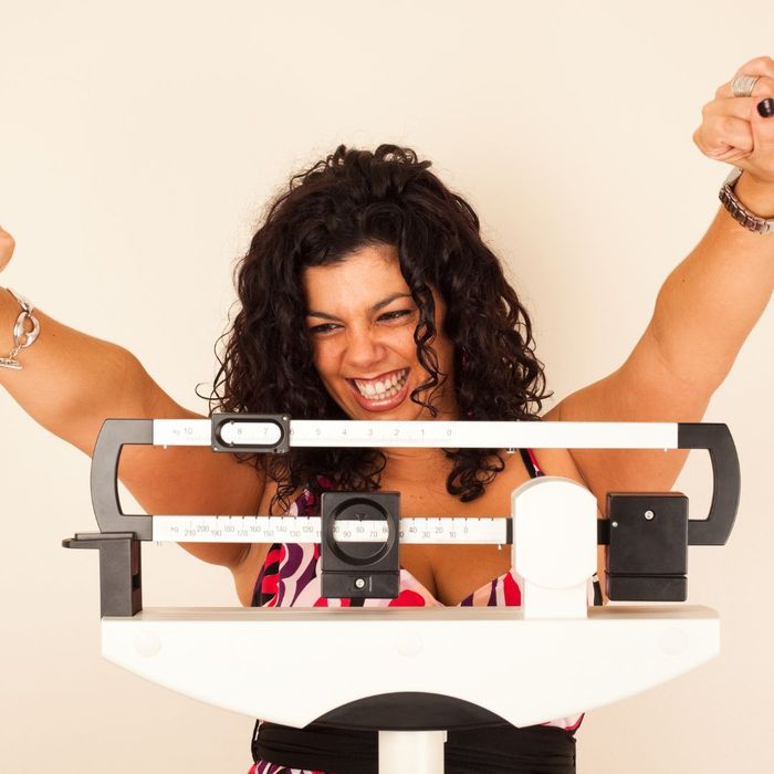 A woman celebrates on a scale after losing weight