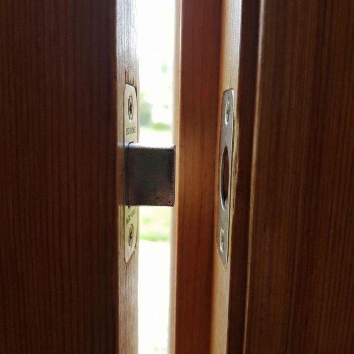 A close-up photograph of a door latch bolt not aligning correctly with the strike plate hole on a wooden door frame.
