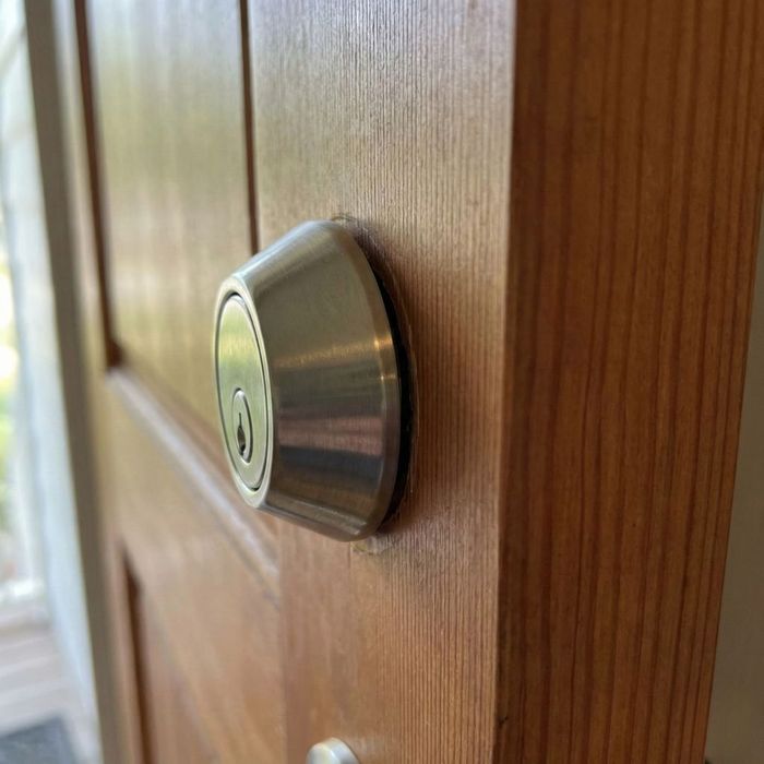 A close-up photograph of a deadbolt lock on a wooden door that does not sit flush against the door surface, showing a visible gap.