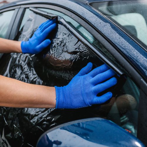 Person wearing blue latex gloves applying new window tint to a vehicle. 