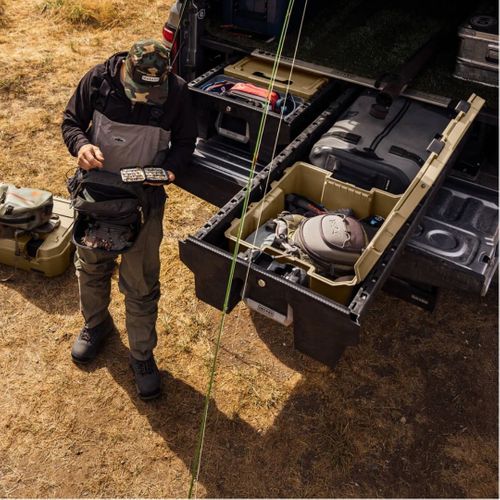 An overhead view of a person standing next to an open truck bed drawer system, which contains various organized gear and equipment, possibly for outdoor adventure or professional work, highlighting the system's capacity and ruggedness.