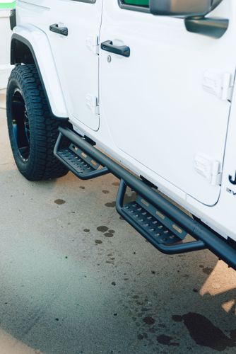 N-FAB drop down step nerf bars installed on a white Jeep Wrangler.