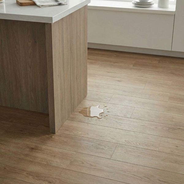 Close-up of waterproof luxury vinyl plank flooring in a kitchen, with a small spill beading on the surface near a kitchen island.