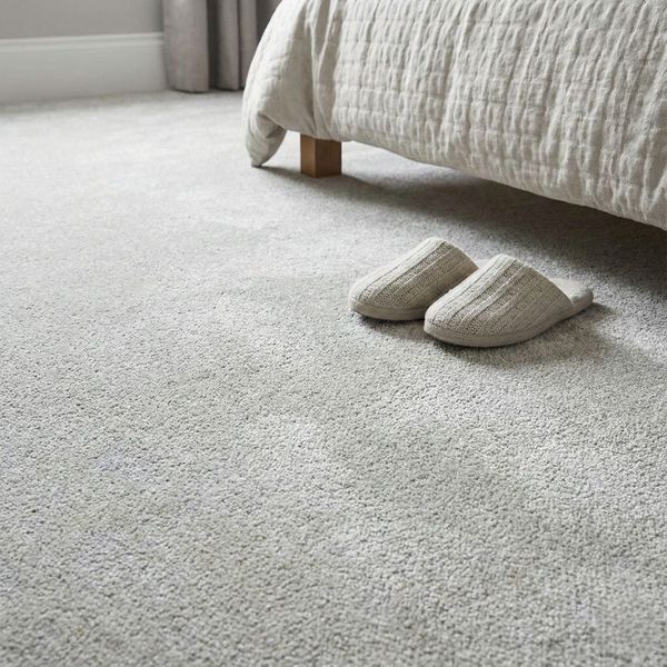 Detailed view of soft, plush light-grey carpeting in a cozy bedroom, with a pair of slippers placed by the bed.