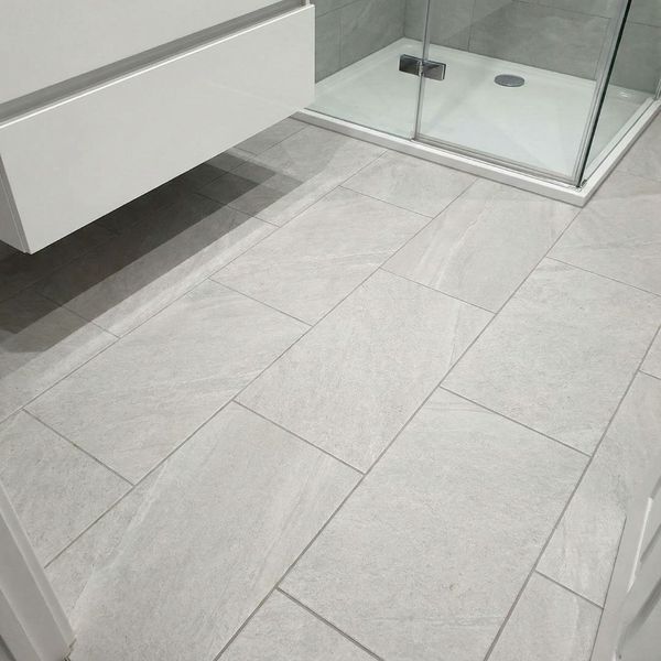A close-up view of a professionally installed grey porcelain tile floor in a modern bathroom, highlighting the clean, precise grout lines and the transition to a shower area.