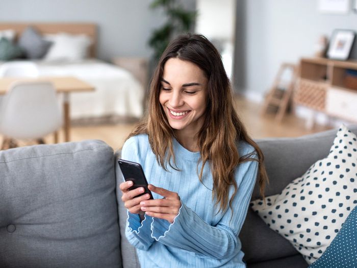 a woman smiling at her phone on the couch