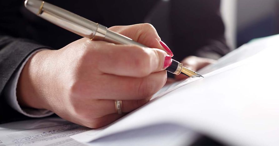 Closeup of a woman's hand holding an ink pen and signing documents