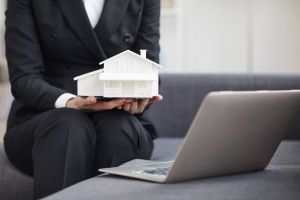 person holding a model house in front of laptop