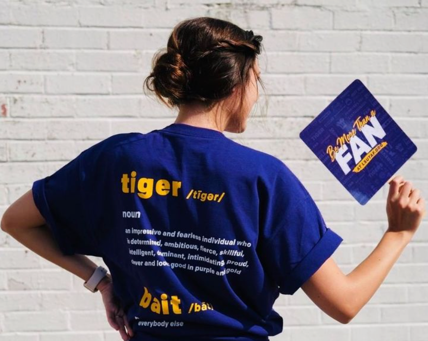 Woman holding a hand sign and wearing a tee both branded 