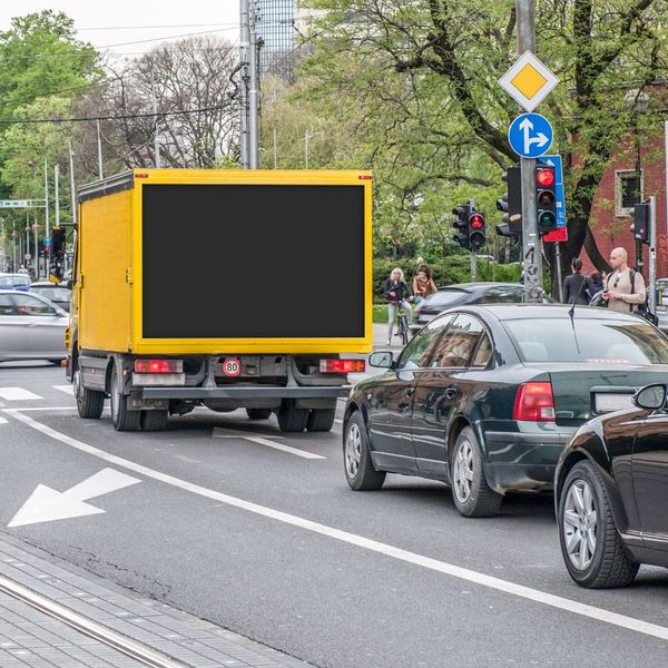Yellow billboard truck with a blank black billboard on the back. 