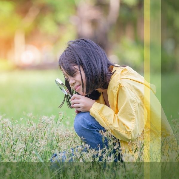 Child Crouching Looking at Plants with Magnifying Glass