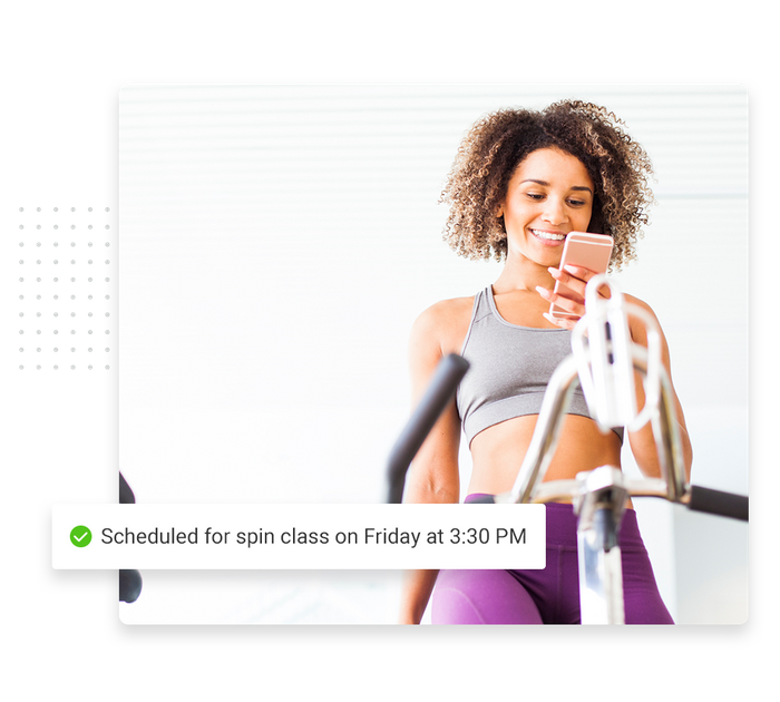 Woman on elliptical with smartphone overlaid with a checkmark that says 'Scheduled for spin class on Friday at 3:30 PM' Fitness scheduling software