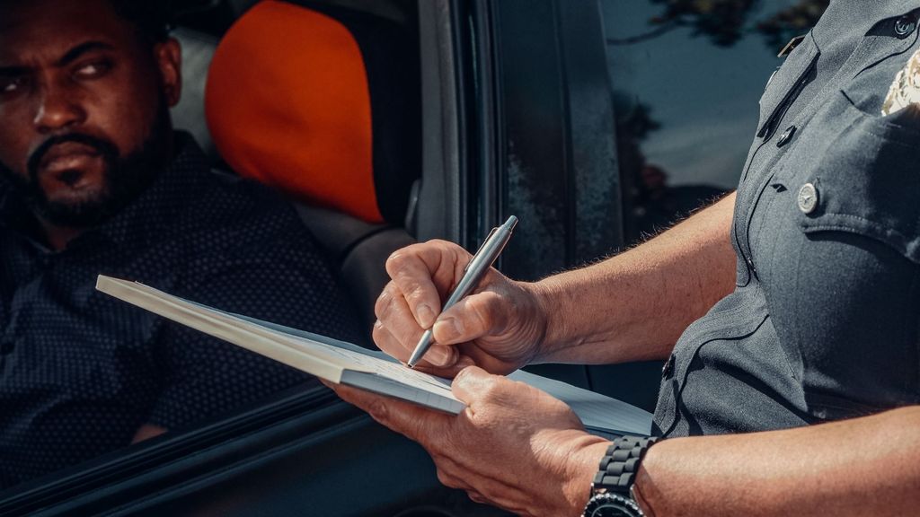 Police officer writing a citation next to a driver in a vehicle during a traffic stop