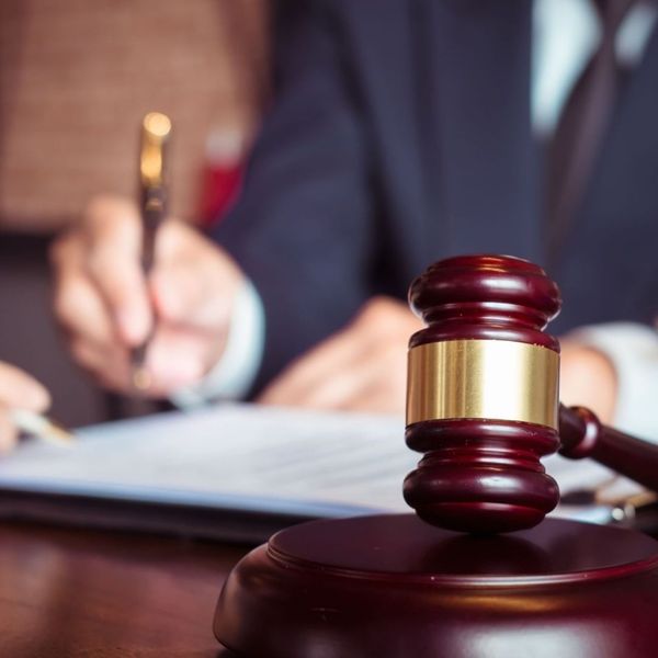 Wooden judge's gavel on a desk with someone reviewing legal documents in the background.