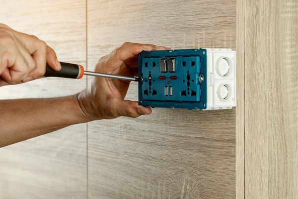someone holding a screw driver up to an outlet