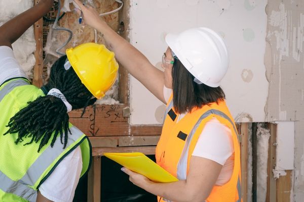 electricians looking at wiring inside of a wall that is under construction