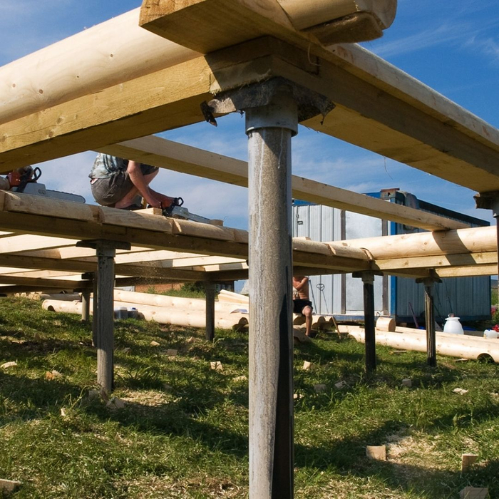 A series of metal adjustable posts supporting a wooden deck or elevated structure from below, with green grass visible.