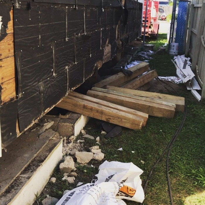 A damaged section of a building's wooden foundation or exterior, with fallen debris and exposed soil.