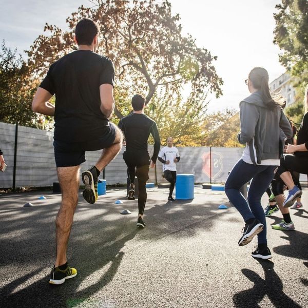 A group of employees participating in an outdoor high-knee cardio drill during a corporate wellness class.