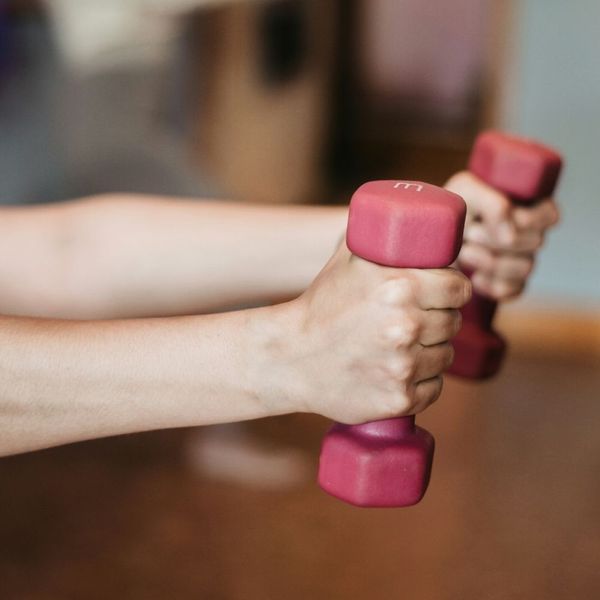 Close-up of a person’s hands holding a pair of pink dumbbells, representing customized strength training and weightlifting programs.