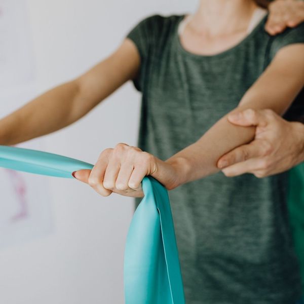 Close-up of a trainer’s hands guiding a client’s arm alignment during a resistance band exercise for corrective therapy.