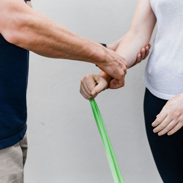 Close-up of a personal trainer's hands assisting a client with proper form and grip during a green resistance band exercise.