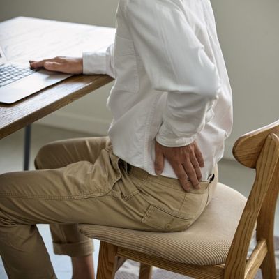 man sitting at desk, holding lower back in pain