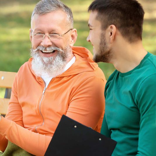 Senior and young man smiling on park bench together