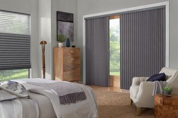 a modern bedroom featuring dark grey honeycomb shades on the main window and vertical shades on the sliding glass door.