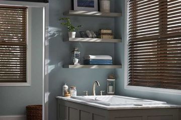 a bathroom with a large bathtub and wood blinds covering two windows.