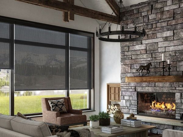 a rustic living room with a stone fireplace and large windows covered by dark, black-out roller shades. a rustic living room with a stone fireplace and large windows covered by dark, black-out roller shades.