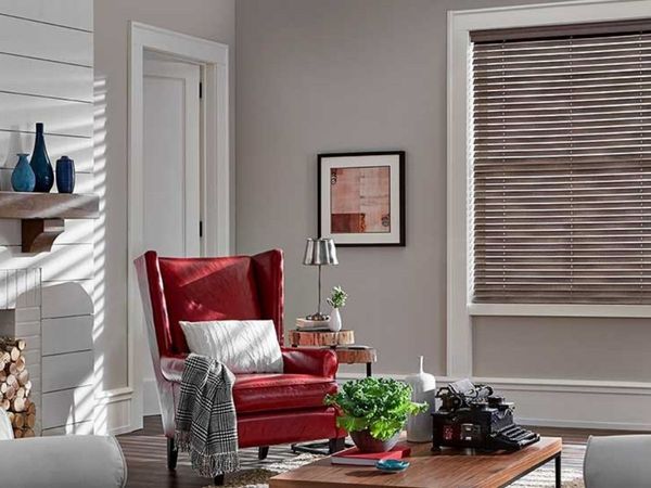 a modern living room featuring a red armchair and faux wood blinds in a rich brown color. a modern living room featuring a red armchair and faux wood blinds in a rich brown color.