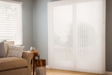 a living room with a couch and large windows covered by sheer, light-filtering window shadings.