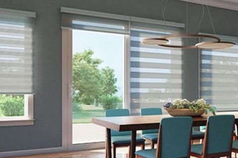 a dining room with a large glass door and window covered by striped light-filtering dual shades.