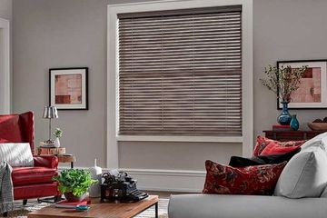 a cozy living room with a red armchair and a window covered by stylish brown faux wood blinds.