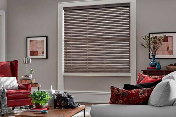 a cozy living room with a red armchair and a window covered by stylish brown faux wood blinds.