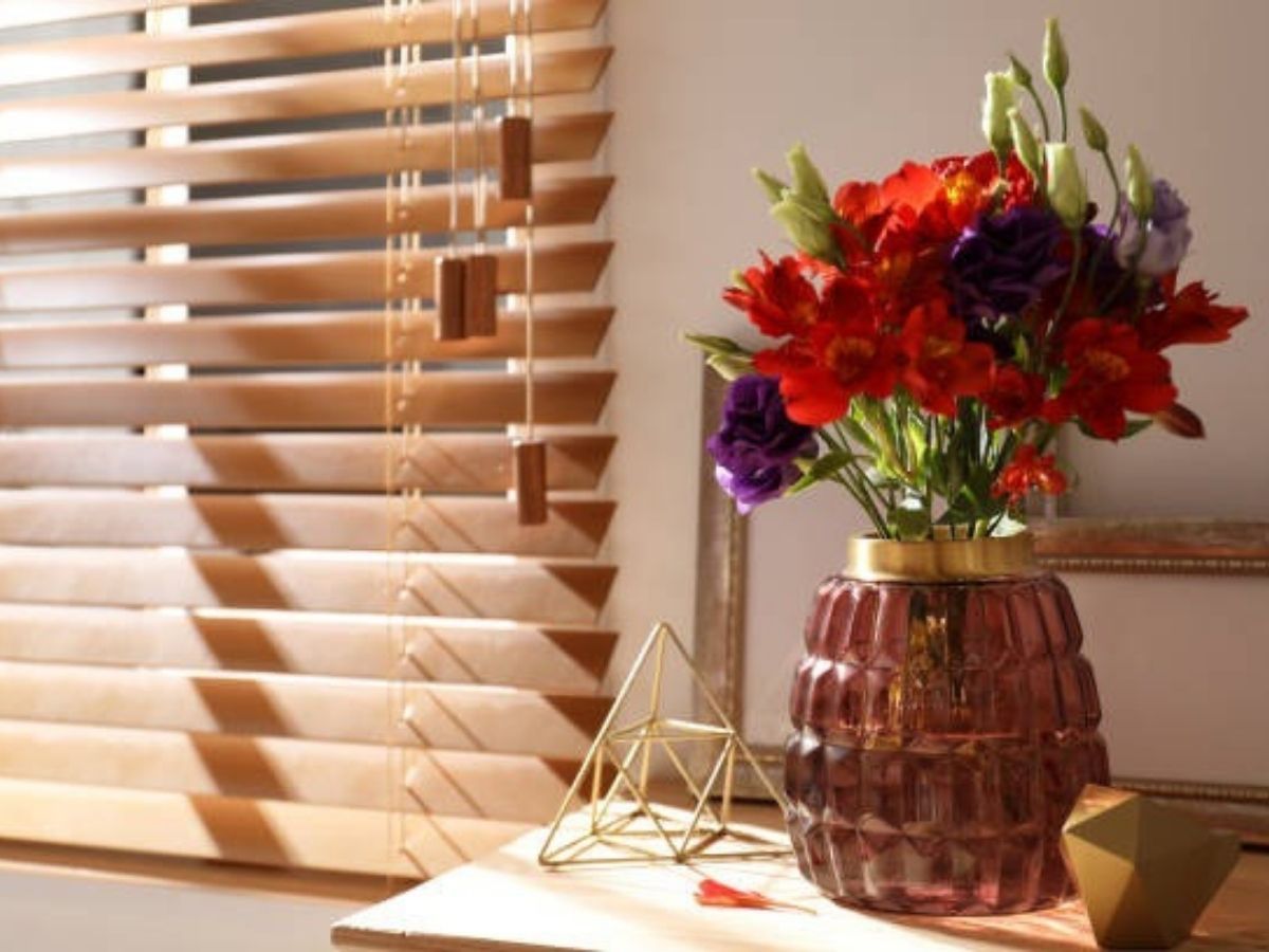 a close-up of a bedside table with a vase of flowers, in front of a window with natural woven blinds. a close-up of a bedside table with a vase of flowers, in front of a window with natural woven blinds.