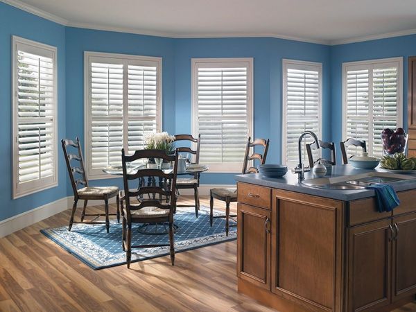 a bright dining area with white custom shutters covering a bay window and kitchen counter space. a bright dining area with white custom shutters covering a bay window and kitchen counter space.